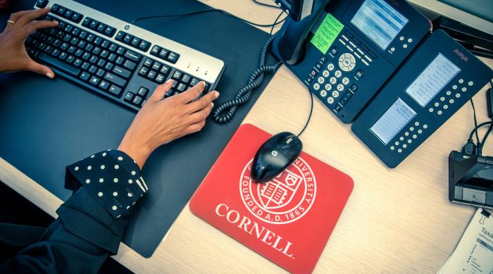 view of woman working with keyboard and computer mousepad reads Cornell